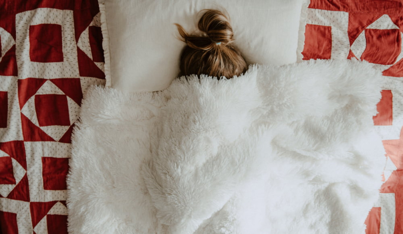 Frau im Bett mit der Decke über dem Kopf